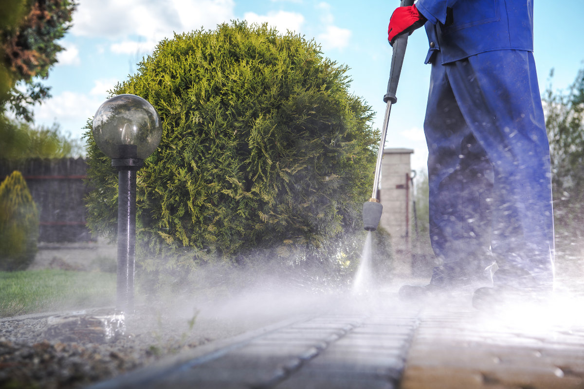 Person power washing or pressure washing to clean pavers near a sidewalk.